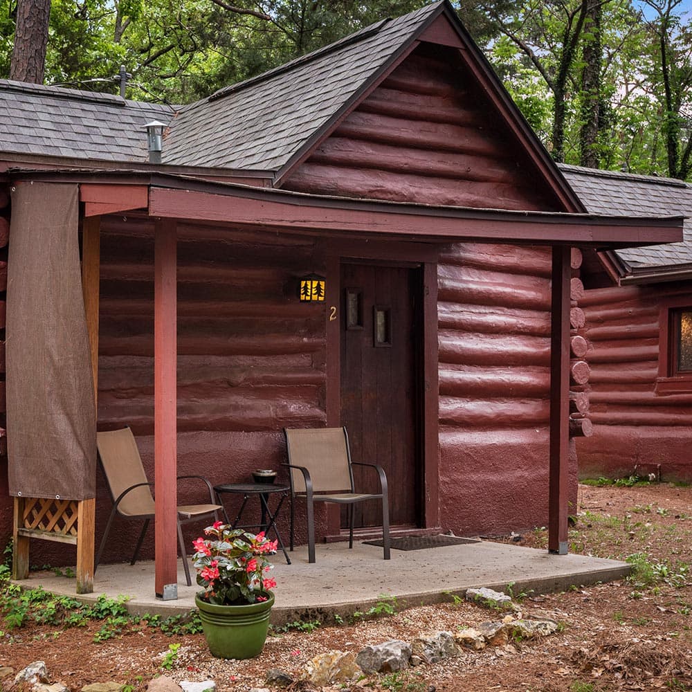 A cozy log cabin with a front porch, two chairs, and a flower pot.
