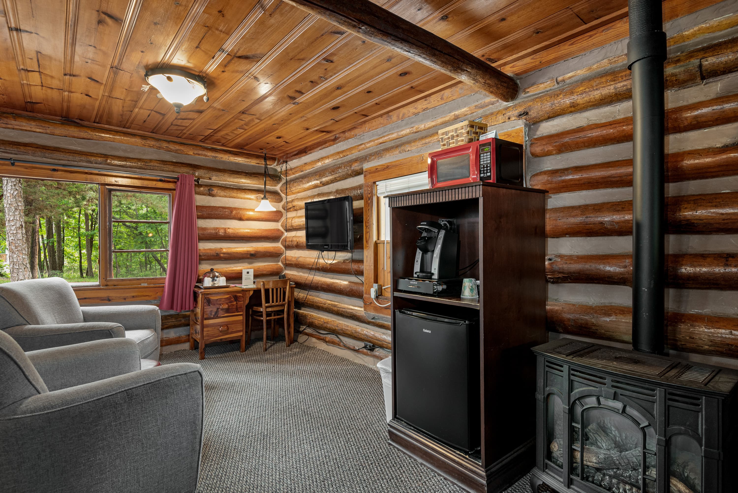 A spacious log cabin bedroom with a king-size bed, two armchairs, a small desk, and a rustic sink area.