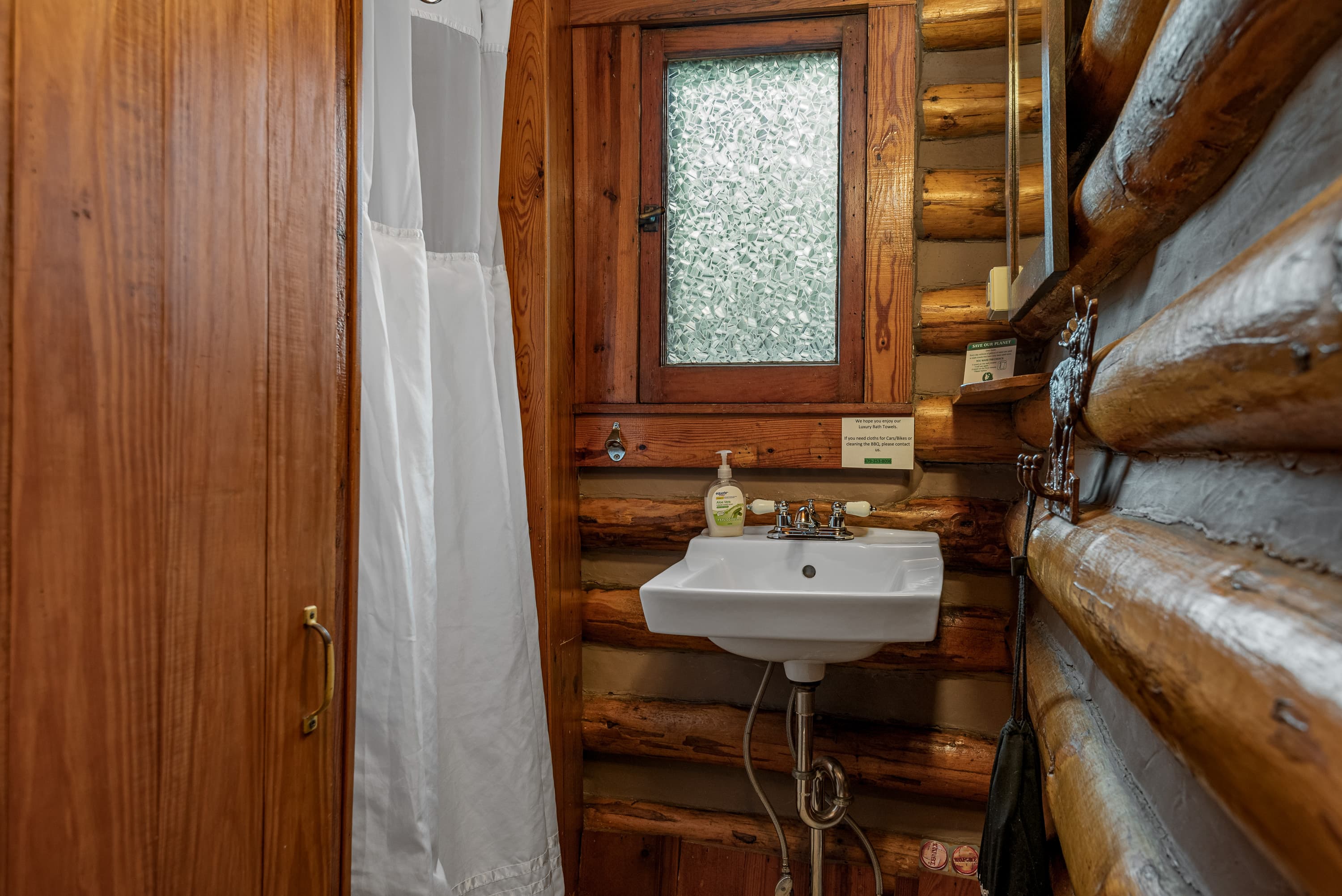 A compact, rustic bathroom features a small white sink and a shower with a white curtain.