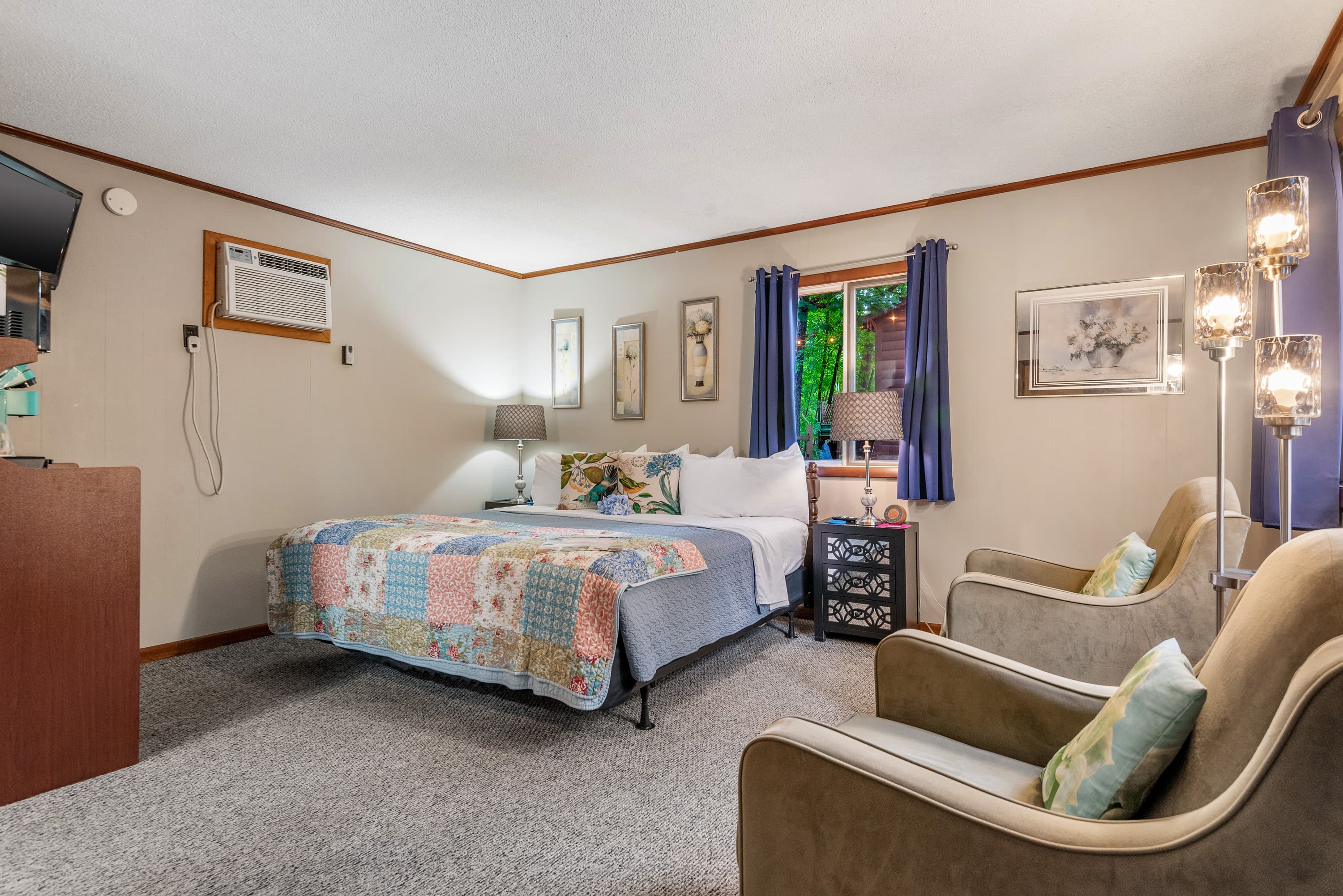 A spacious bedroom features a king-size bed with light-blue bedding, two end tables with lamps, and framed art.