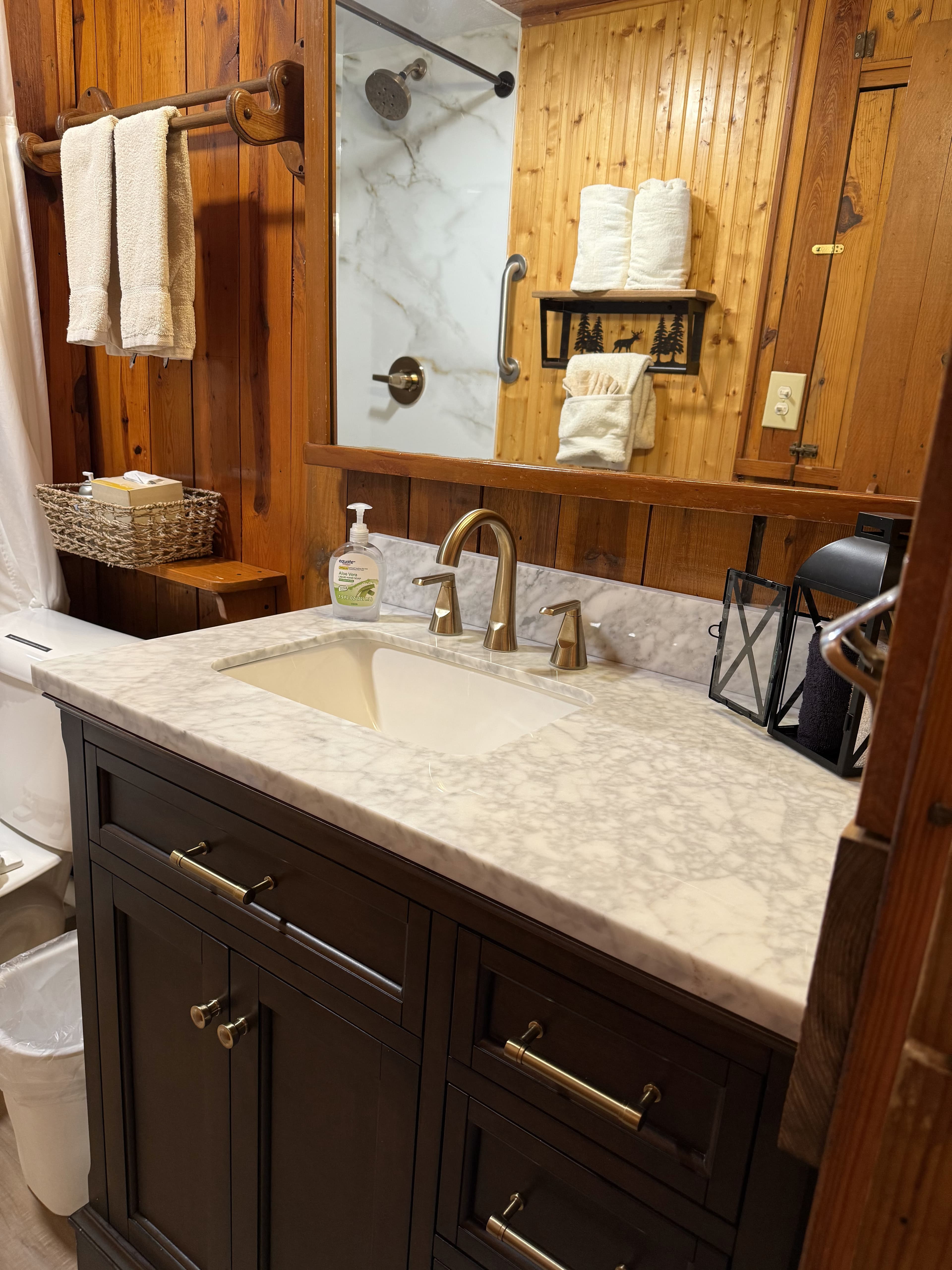 A rustic bathroom with marble sink, dark wood vanity, towels, and wood-paneled walls