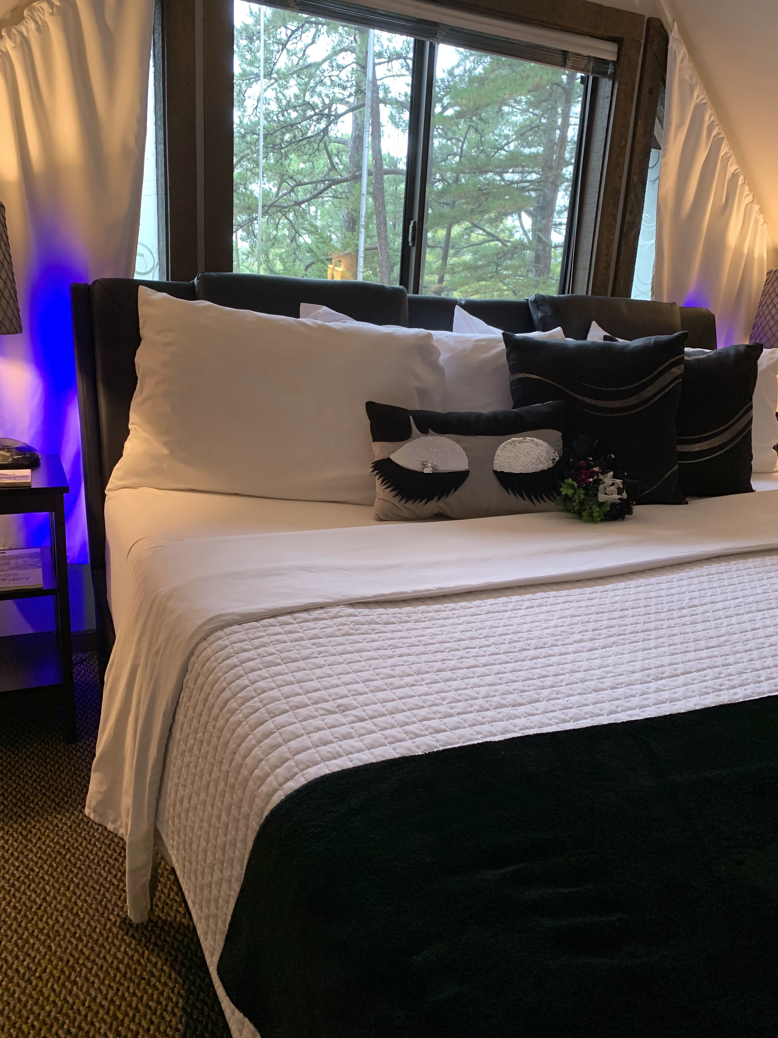A close-up of a bed with black and white bedding. The pillows have a modern, circular design, and there are blue lights on the headboard.