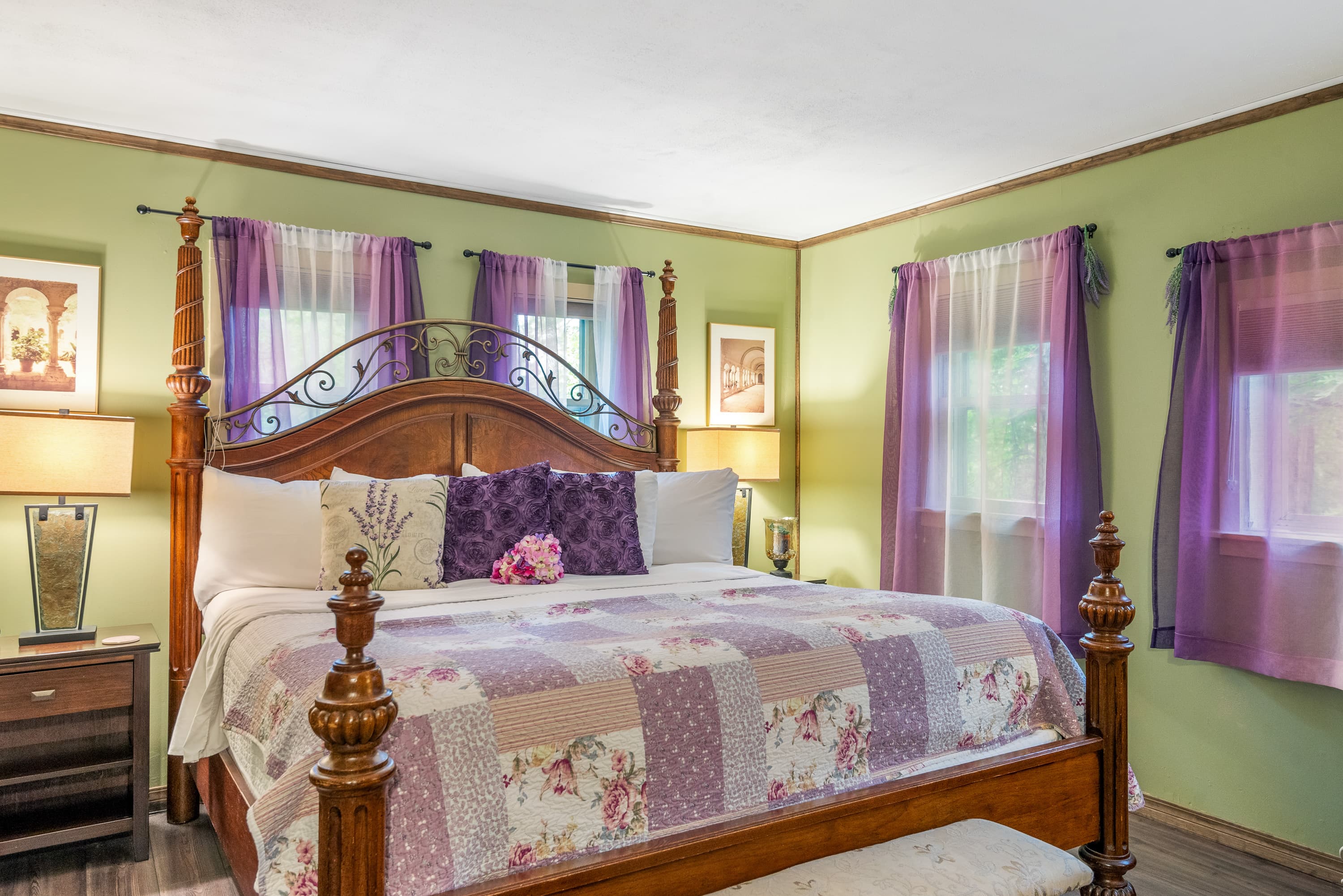 A king-size, four-poster bed with a colorful quilt and pillows dominates a bedroom with lime-green walls and sheer purple curtains.