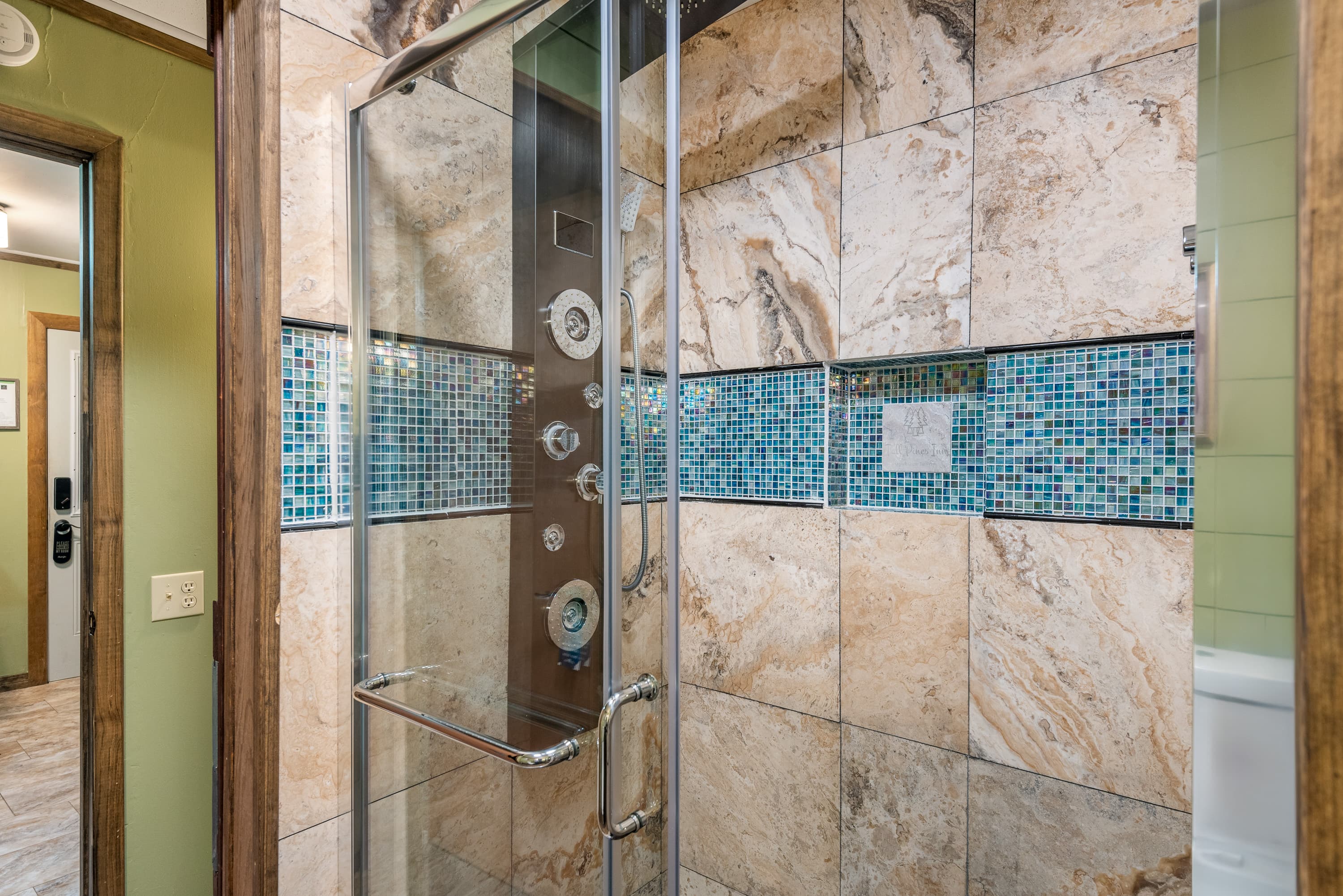 A walk-in shower with glass doors features multi-colored tile and a stylish blue mosaic border, with a shower tower for jets.