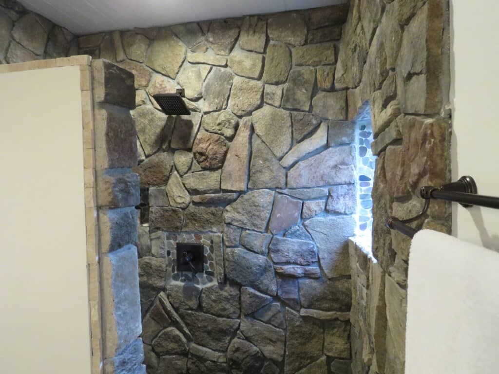 A stone-walled shower with a window and a showerhead mounted on the ceiling.