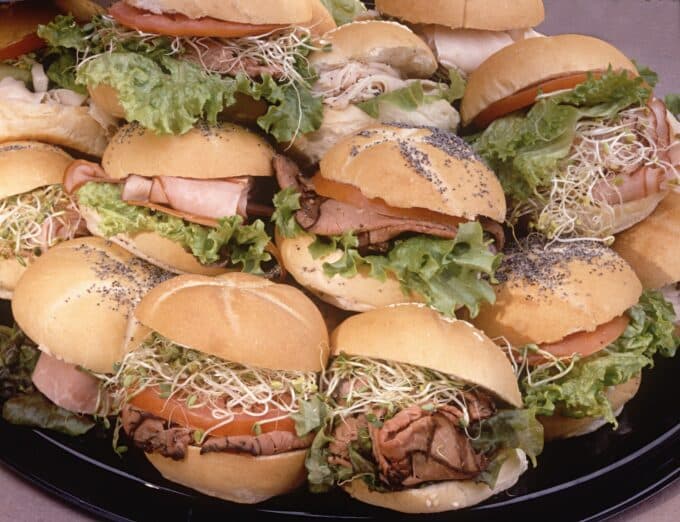 A close-up of a platter stacked with assorted mini sandwiches featuring lettuce, tomato, and various meats.