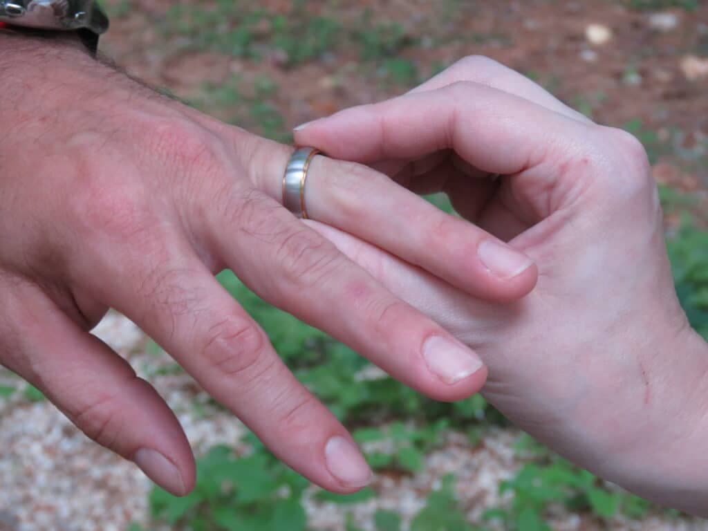 A close-up of a male hand wearing a ring reaching out to touch a female hand.