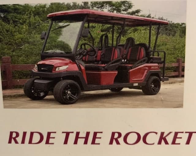 A red and black utility vehicle parked on a path surrounded by greenery.