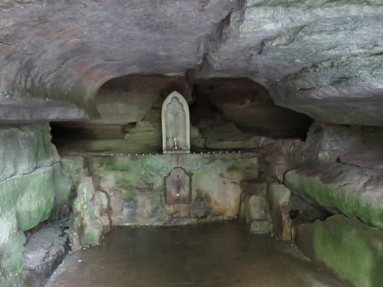 A stone altar with a statue is situated inside a dimly lit cave.