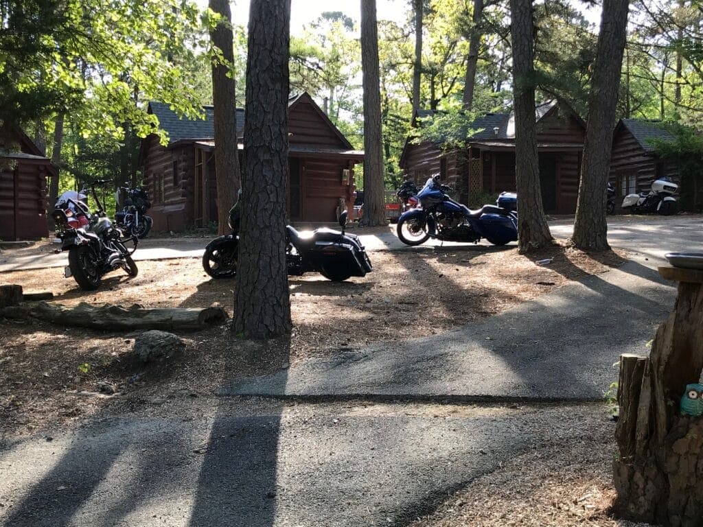 Motorcycles parked near rustic log cabins in a wooded area.
