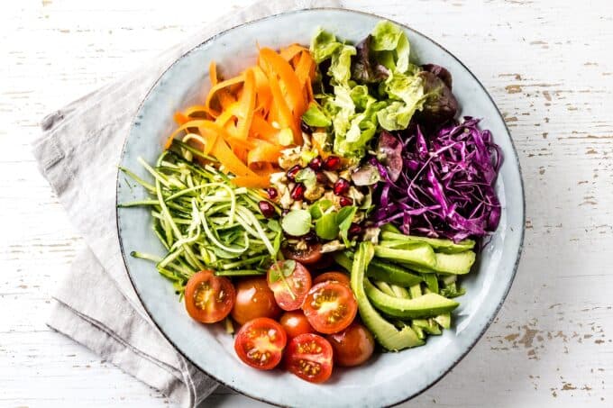 A colorful assortment of fresh vegetables including carrots, lettuce, red cabbage, zucchini, tomatoes, and cucumber arranged in a round bowl.
