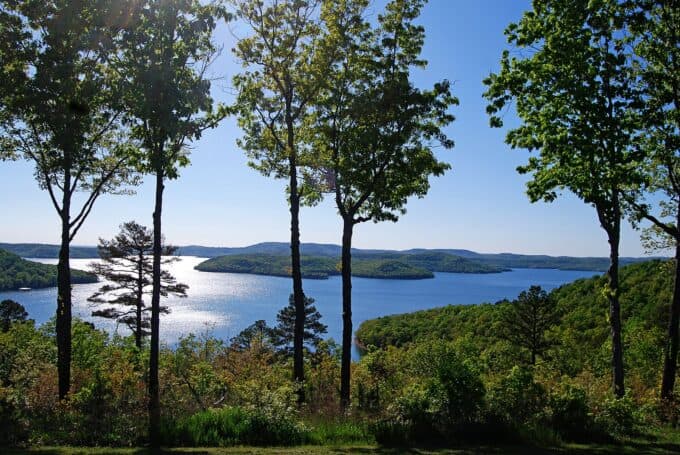 A scenic view of a lake surrounded by green hills and trees under a clear blue sky.