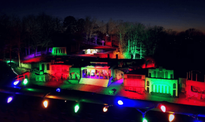 A miniature village illuminated with vibrant red, green, and blue lights against a twilight backdrop.