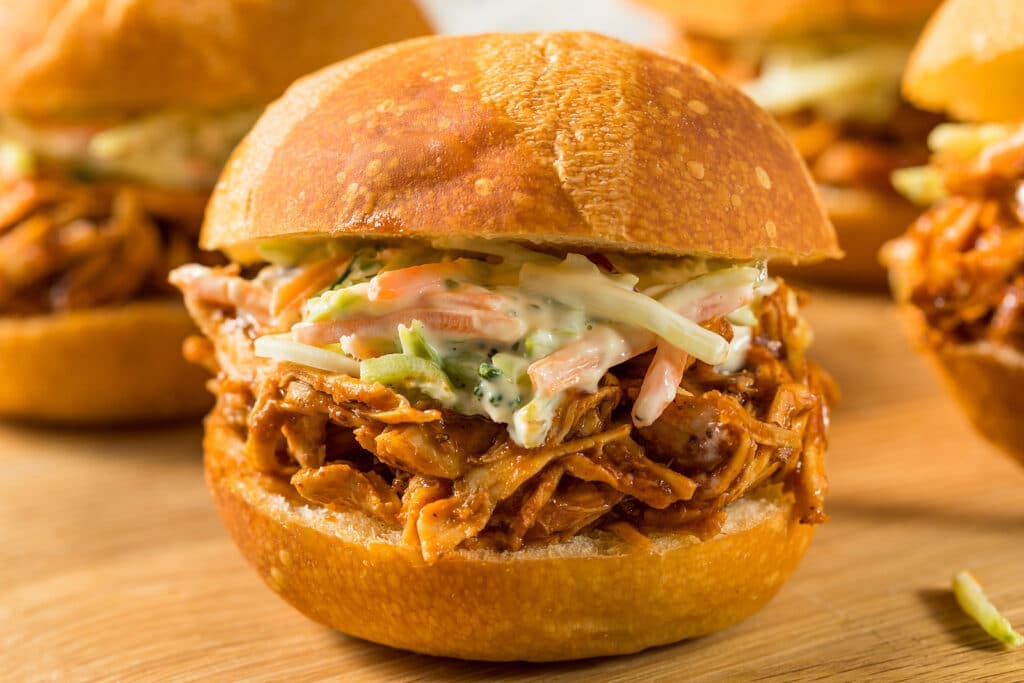 A close-up of a pulled pork sandwich topped with coleslaw on a wooden surface.
