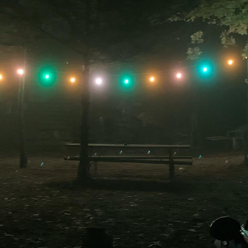 A dimly lit outdoor space with colorful string lights and a picnic table surrounded by fog.