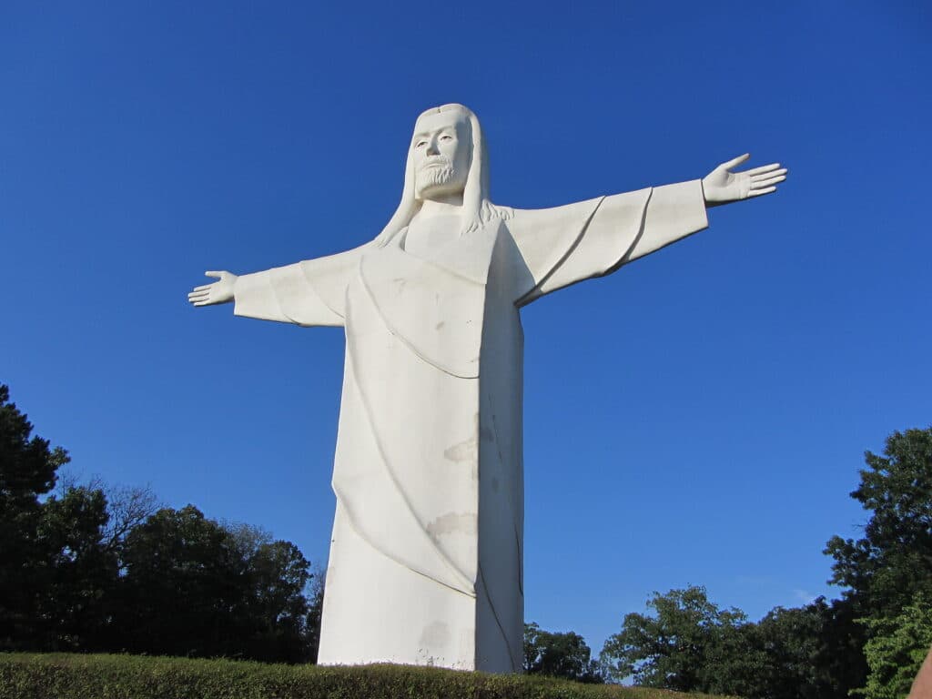 A large white statue of Jesus Christ with outstretched arms against a clear blue sky.