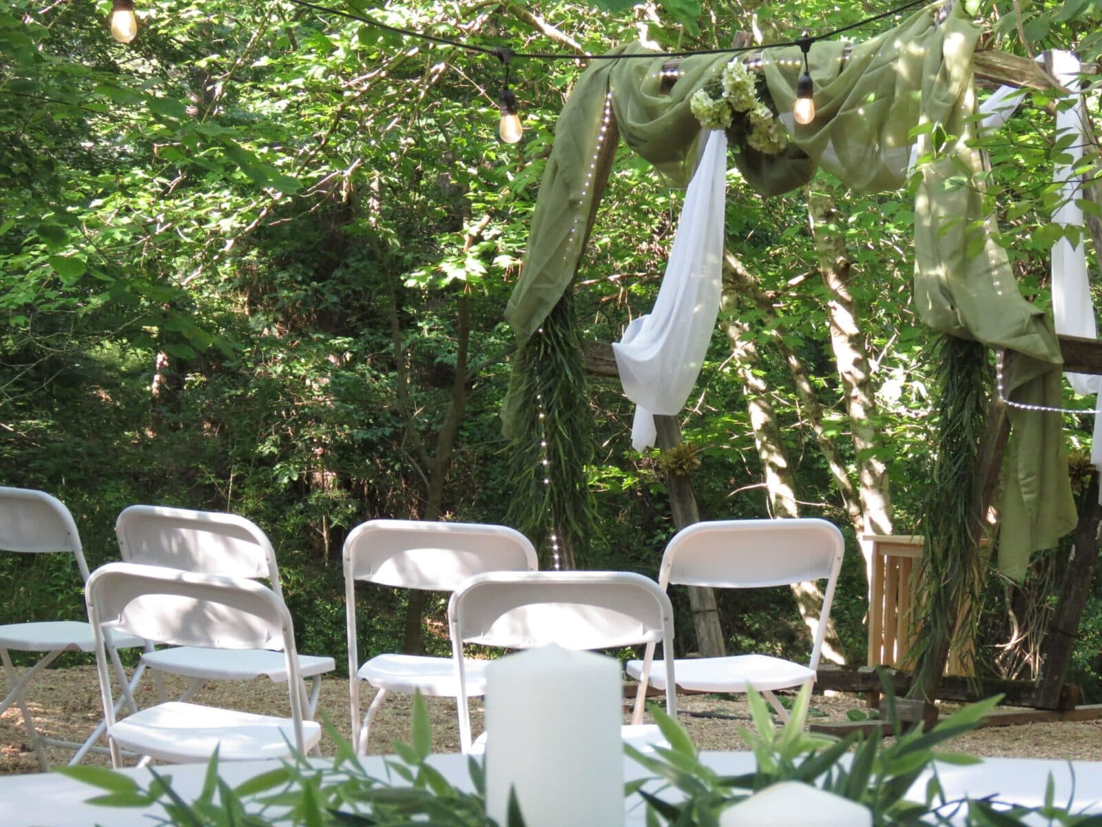 An outdoor wedding setup with white chairs, draped fabric, and decorative greenery.
