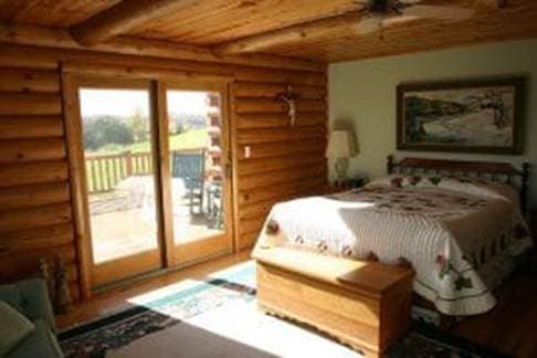 A cozy log cabin bedroom featuring a bed, a chest, and large sliding glass doors leading to a patio.