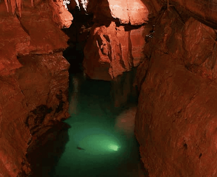 A subterranean river flows through a deep, reddish canyon illuminated by soft lighting.