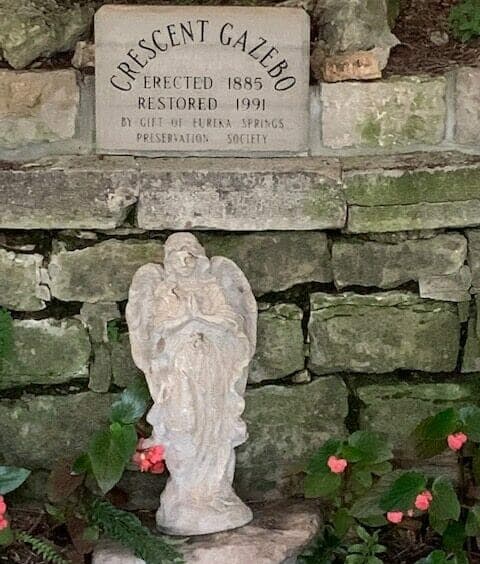 A stone angel figurine stands in front of a plaque reading "Crescent Gazebo, Erected 1885, Restored 1991."