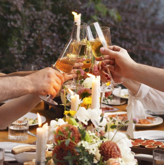 A group of hands clink champagne glasses in celebration at a beautifully set dinner table.