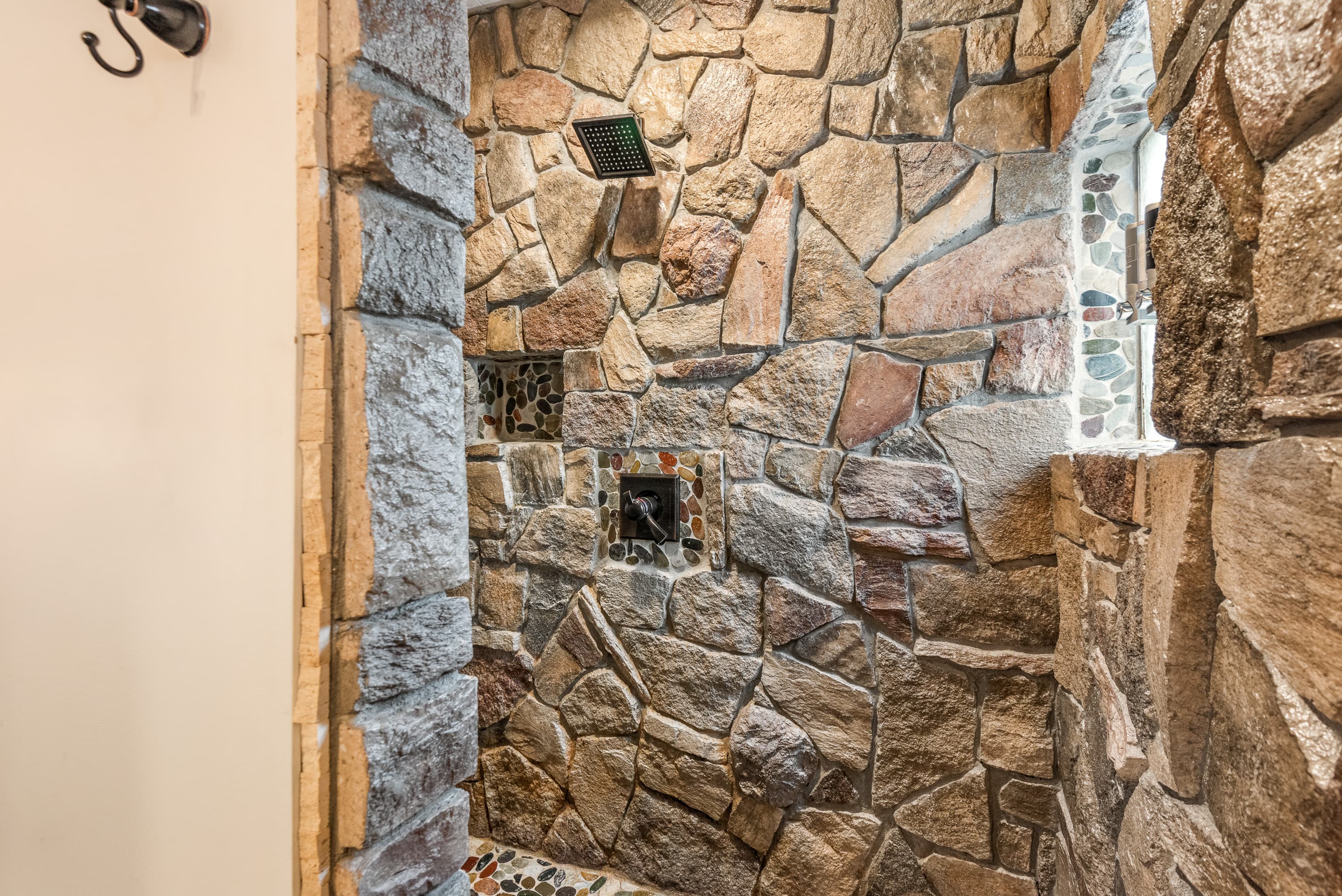 A close-up view of a walk-in shower with stone walls in various shapes and sizes. A rain showerhead and a soap dish are visible.