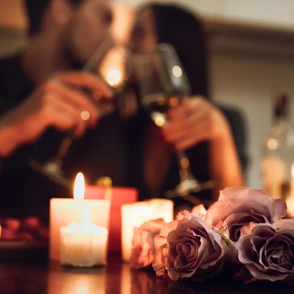 A couple toasts with wine glasses surrounded by candles and roses.