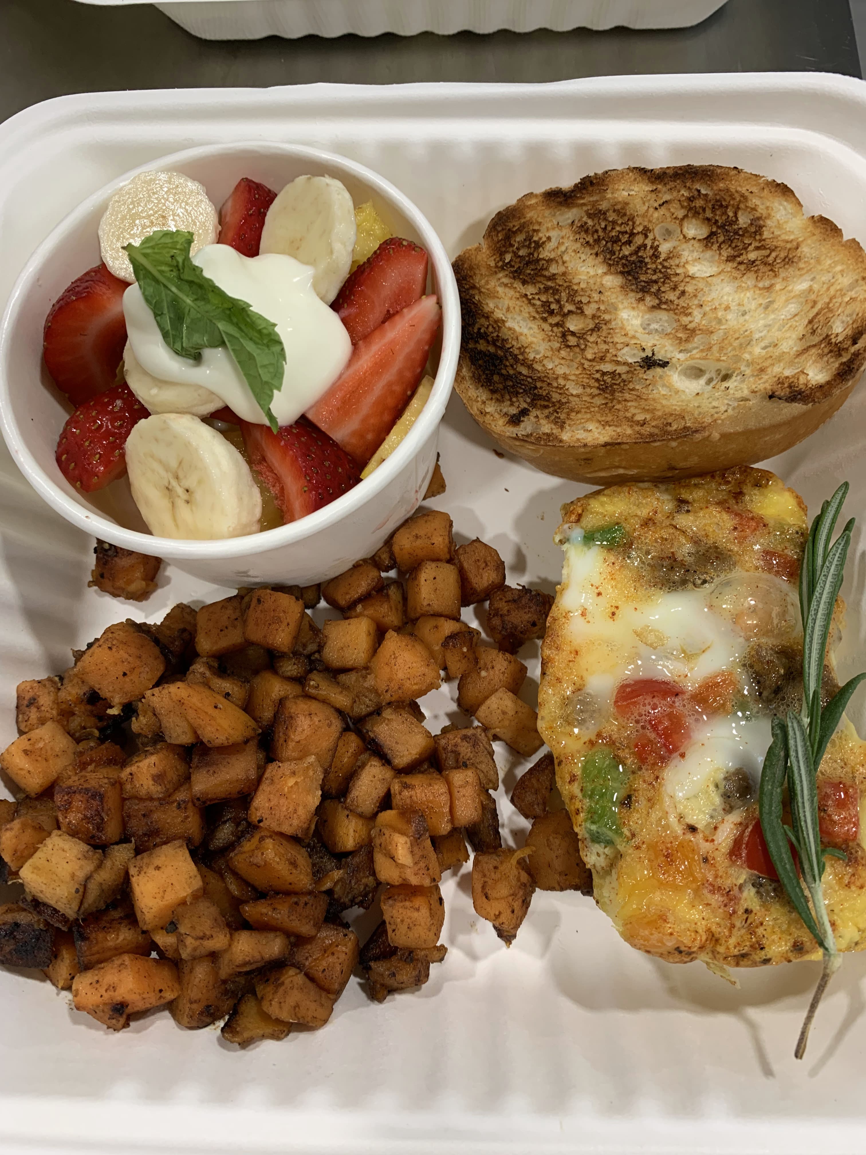 A meal featuring a fruit cup, seasoned diced potatoes, an omelet, and toasted bread.