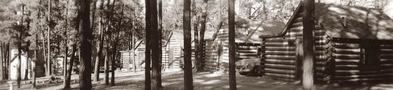 Black and white photo of log cabins nestled among trees.