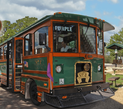 A green and wooden trolley bus labeled "PURPLE" parked in a sunny outdoor area.
