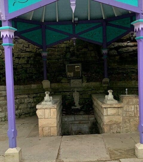 A colorful gazebo with stone benches and a plaque, set against a rocky backdrop.
