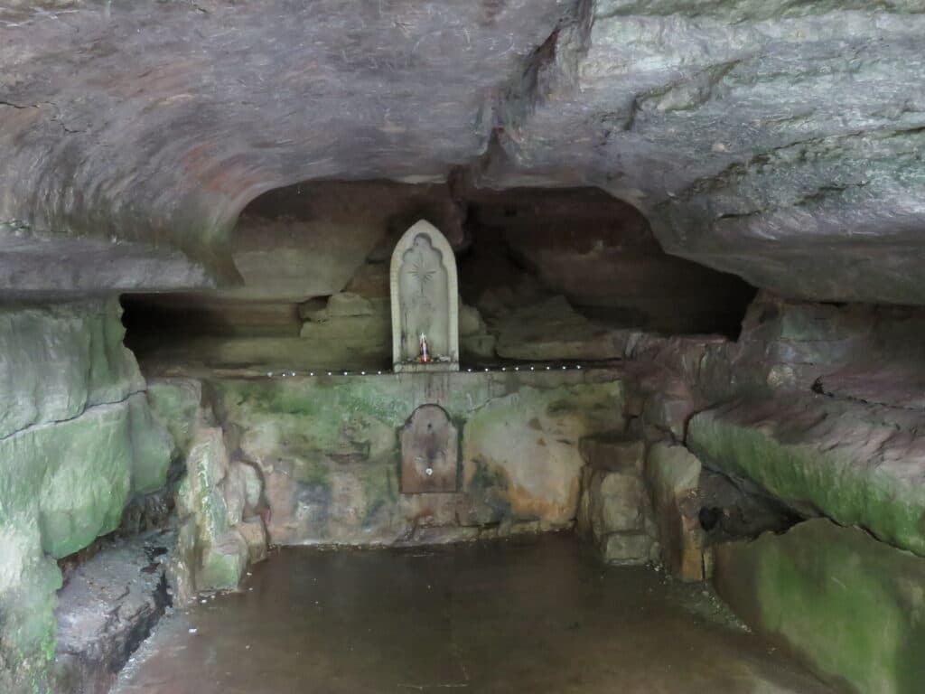 A small shrine with an idol is set against the rocky walls of a cave.