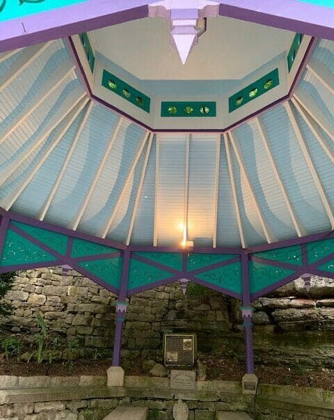 View of a brightly colored gazebo's interior with decorative beams and a stone backdrop.