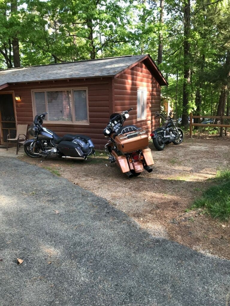 Three motorcycles parked outside a rustic cabin surrounded by trees.