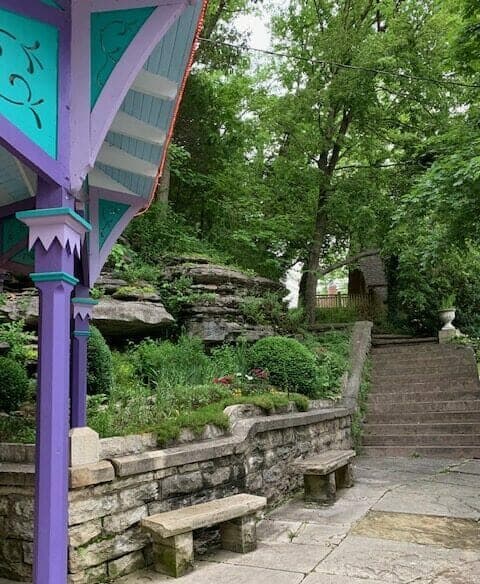 A colorful gazebo stands beside a stone pathway leading up to a lush, green garden.