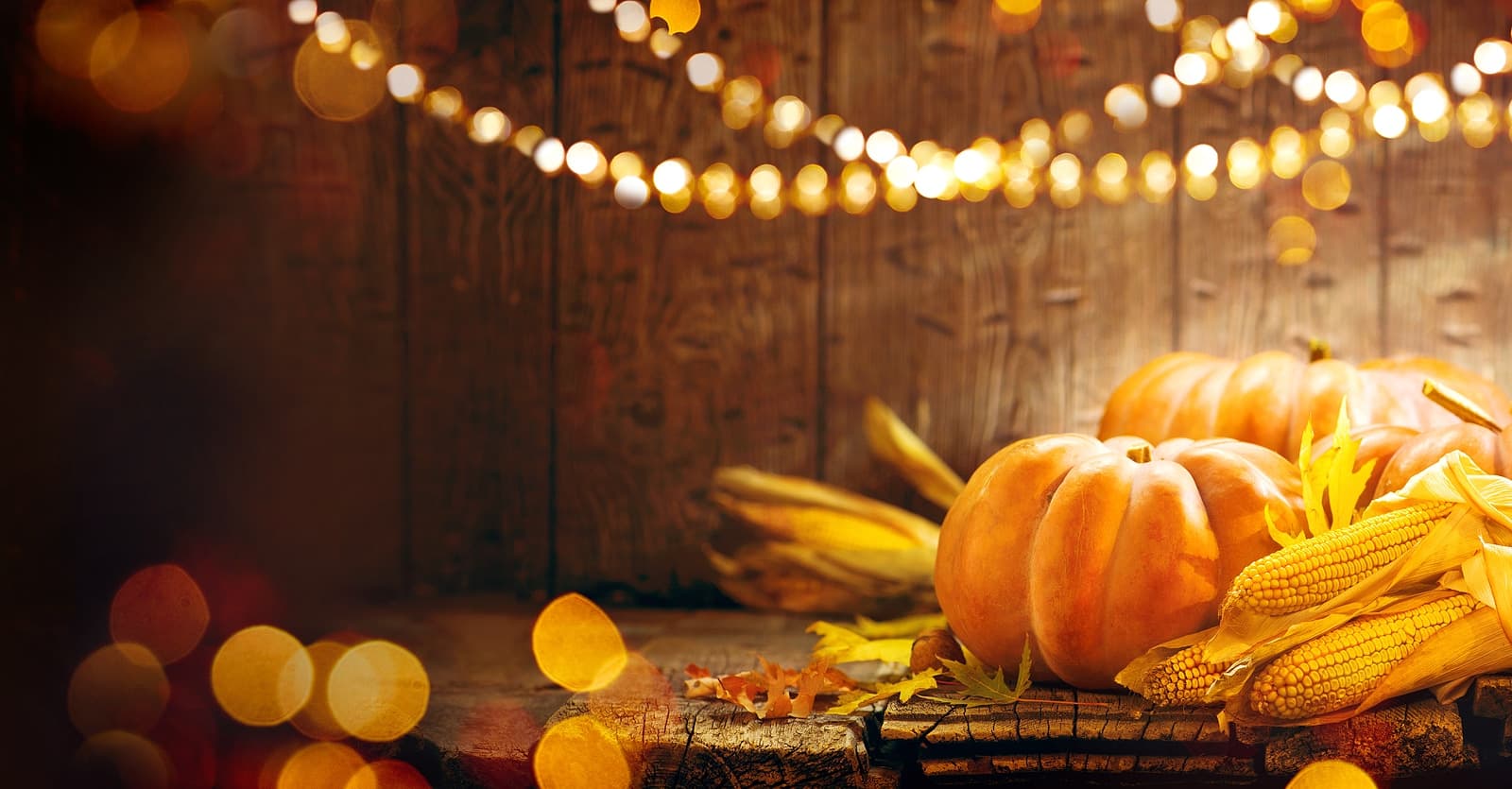 A cozy autumn scene featuring pumpkins, corn, and warm lighting against a wooden backdrop. A cozy autumn scene featuring pumpkins, corn, and warm lighting against a wooden backdrop.