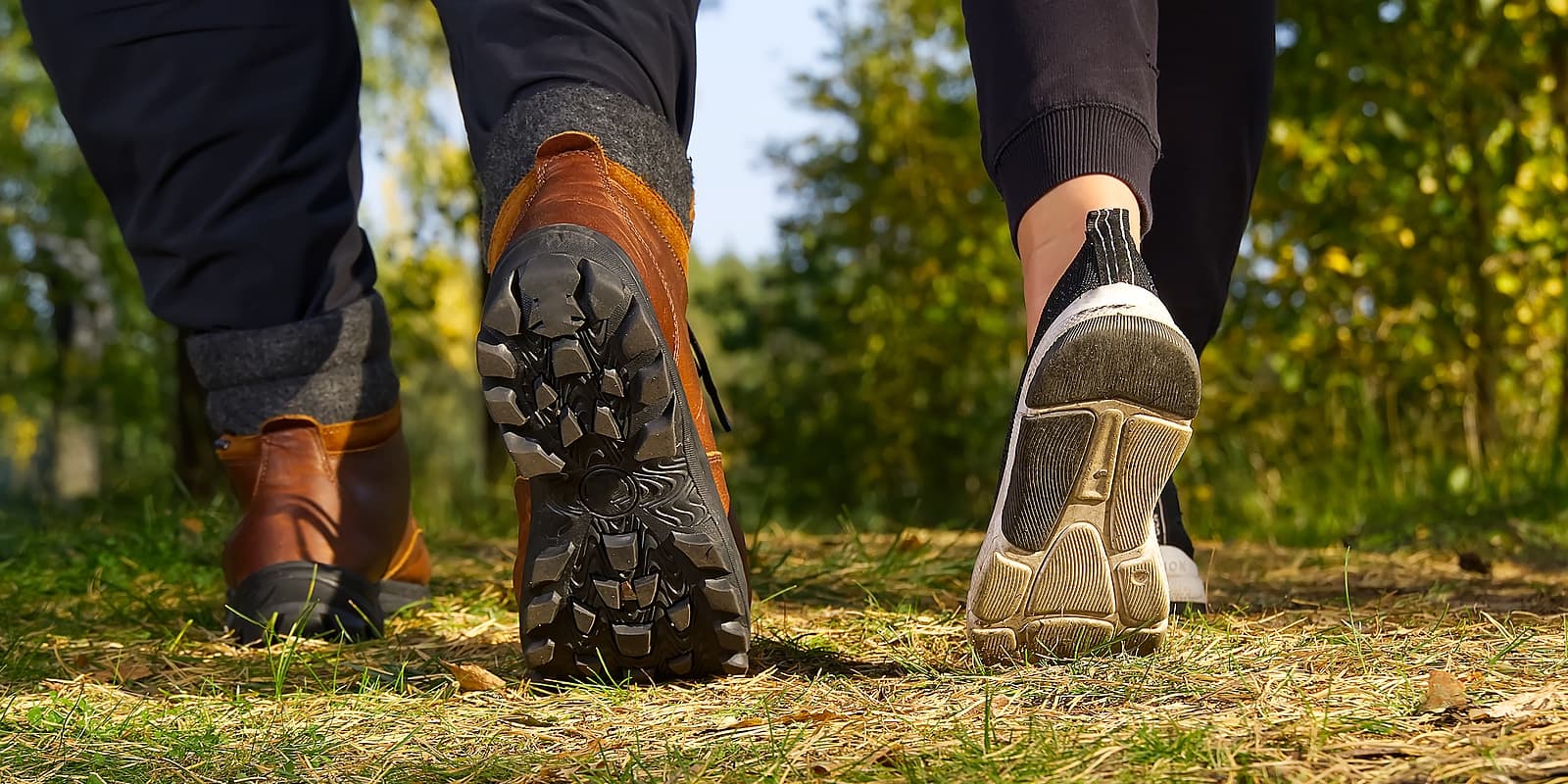 Two pairs of shoes walking on a grassy path in a wooded area.