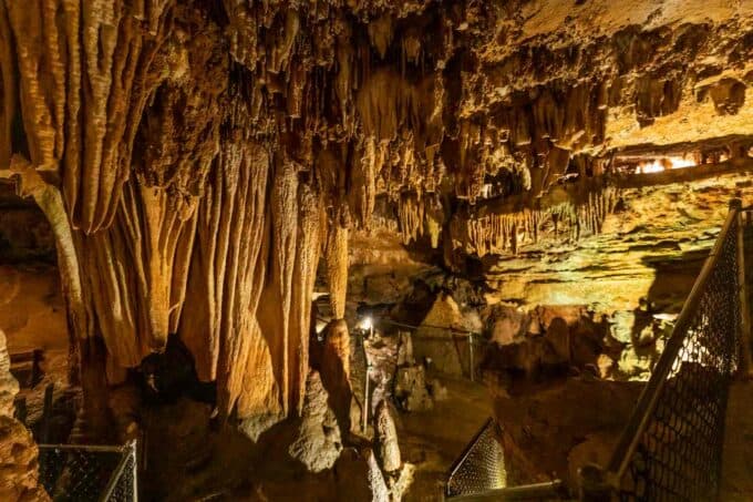A rock cave interior featuring stalactites and stalagmites illuminated by soft lighting.