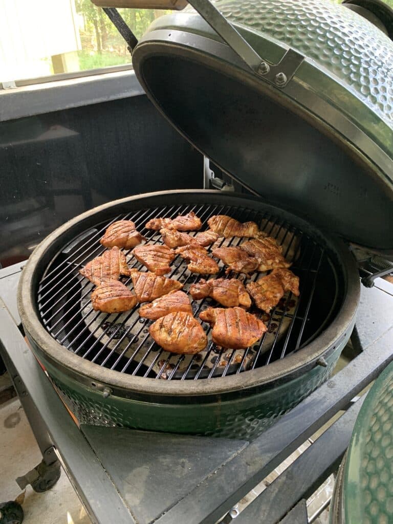 Grilled chicken pieces are cooking on a green ceramic barbecue grill.