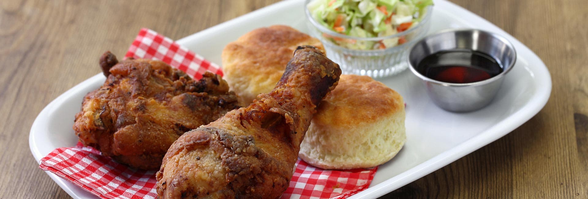 A plate of crispy fried chicken, two biscuits, coleslaw, and a small bowl of sauce.