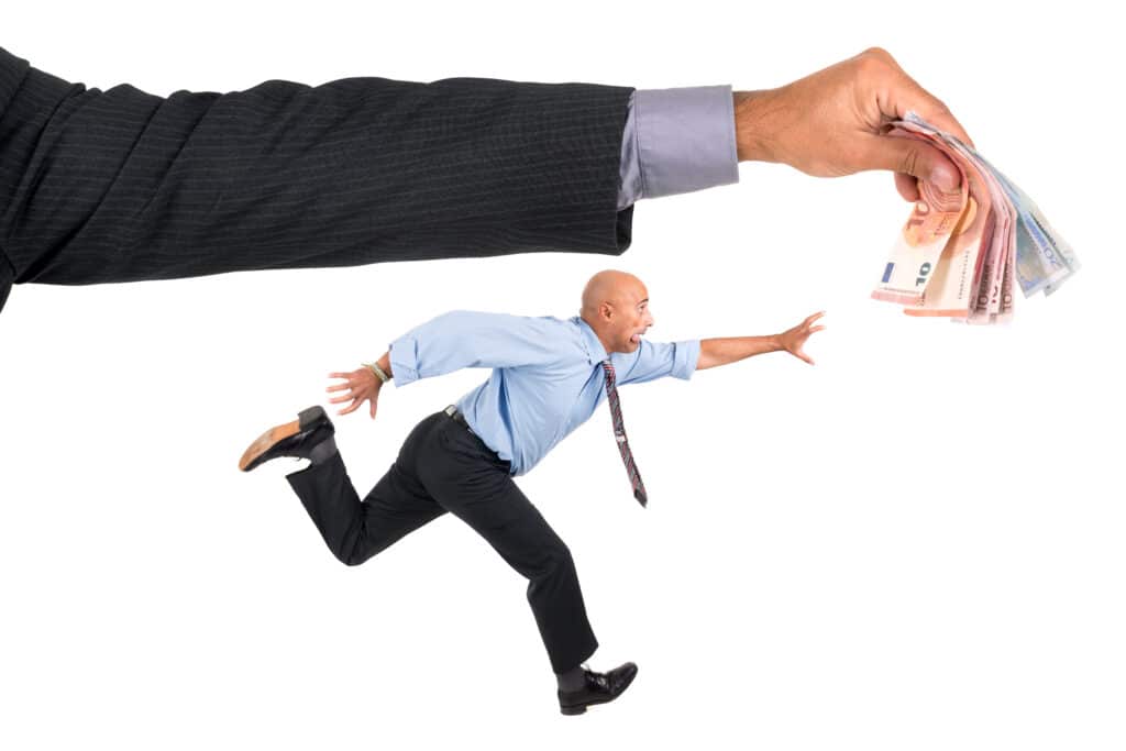 A businessman frantically runs away while reaching for money held by a large hand.