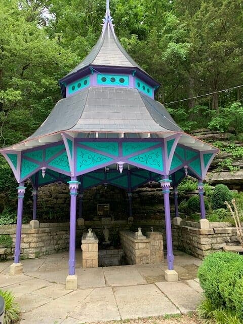A decorative gazebo with purple and turquoise accents surrounded by lush greenery.