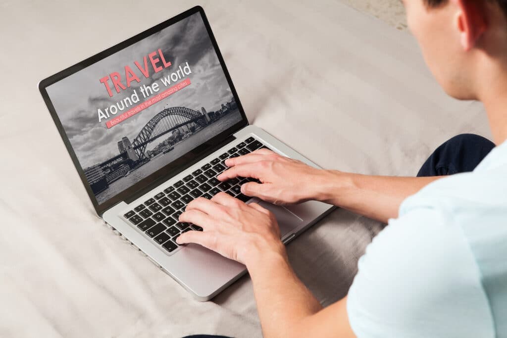 A person uses a laptop to browse a travel website featuring a photo of a bridge.