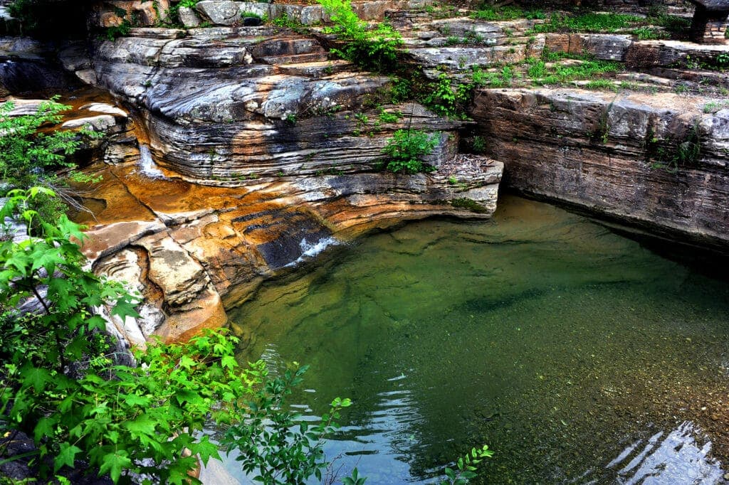 A tranquil pool of clear water surrounded by textured rock formations and lush greenery.