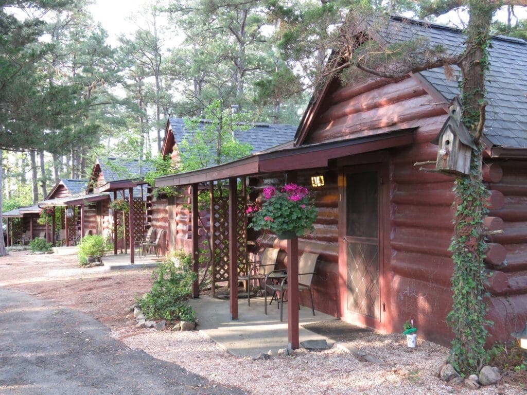A row of rustic log cabins surrounded by trees and flower planters.
