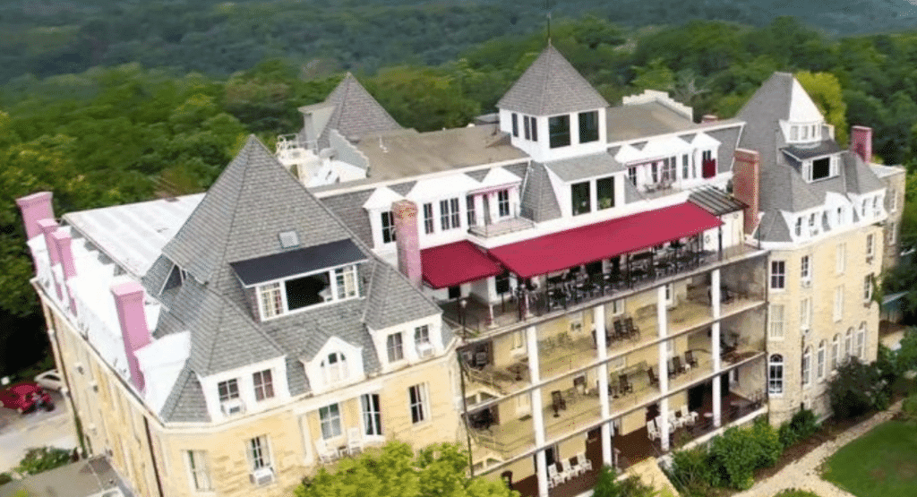 Aerial view of a large, ornate building with multiple pointed roofs and a red awning over a spacious balcony.