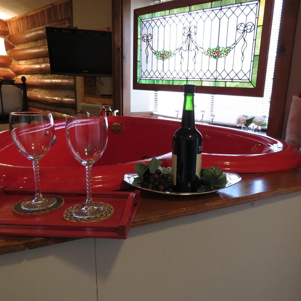 A romantic setting featuring a red hot tub, two wine glasses, a bottle of wine, and a decorative stained glass window.
